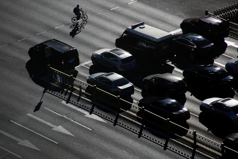 FILE PHOTO: A cyclist rides past cars that are waiting at a traffic light in central Beijing