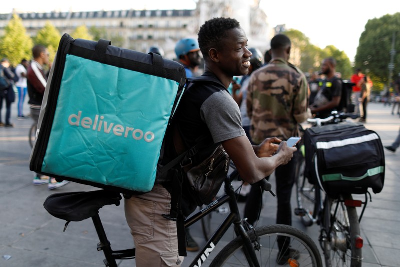 A biker, wearing a Deliveroo food courier backpack, demonstrates during a call on clients to