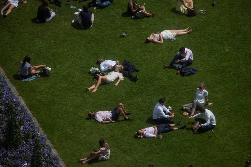 FILE PHOTO: Workers sit on green during a lunch break as they enjoy the hot weather in London