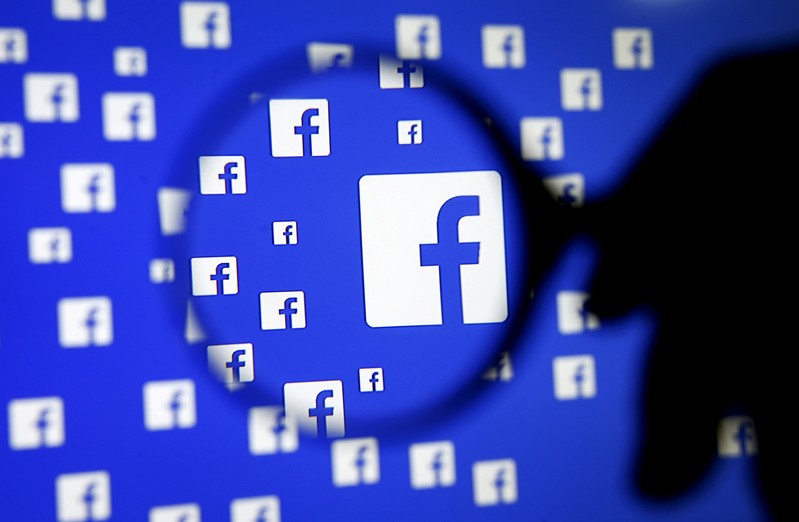 FILE PHOTO: A man poses with a magnifier in front of a Facebook logo on display in this