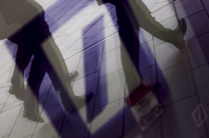 Pedestrians are reflected in a window as they walk in front of the headquarters of Deutsche