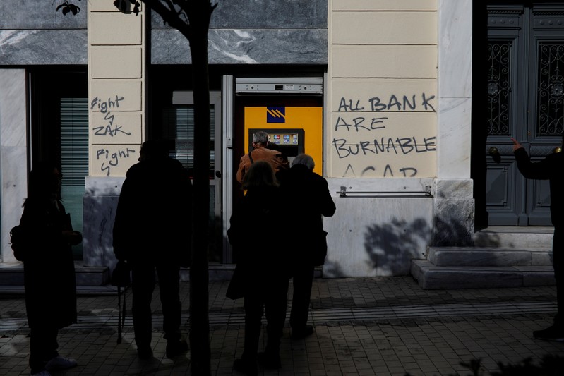 FILE PHOTO: People line up at an automated teller machine outside a Piraeus Bank branch in