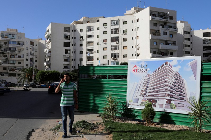 A man walks npast a banner advertising for buildings that will be built, in Tripoli