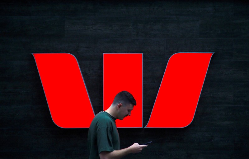 FILE PHOTO: A pedestrian looks at his phone as he walks past a logo for Australia's Westpac