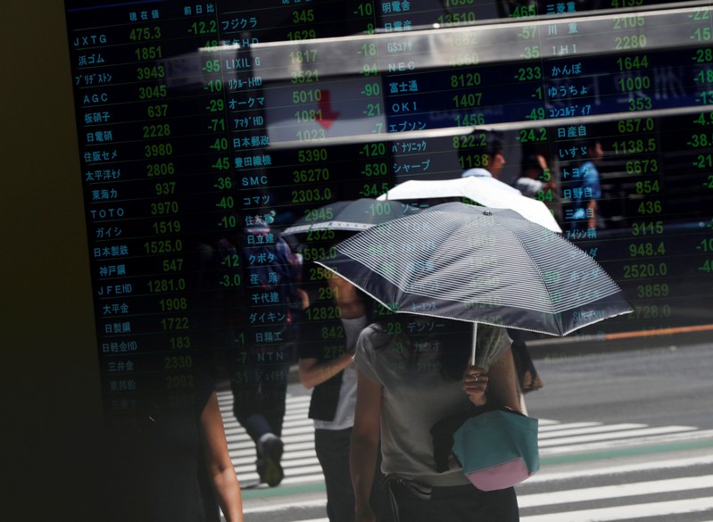 Passersby are reflected on a stock quotation board outside a brokerage in Tokyo