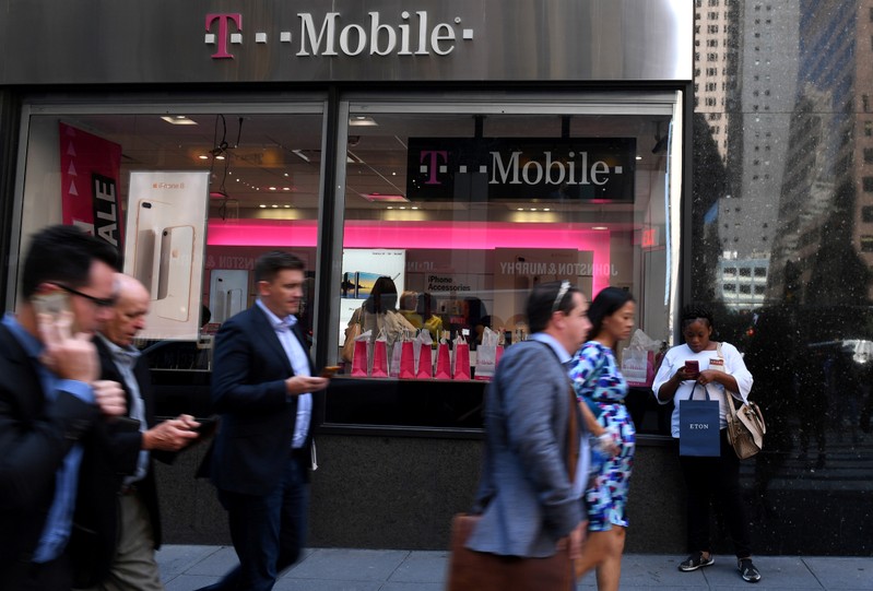 Pedestrians use their smart phones as they pass a T-Mobile retail store in New York City