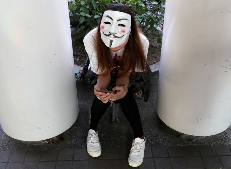 FILE PHOTO: An anti-government protester wearing a Guy Fawkes mask checks her phone during the