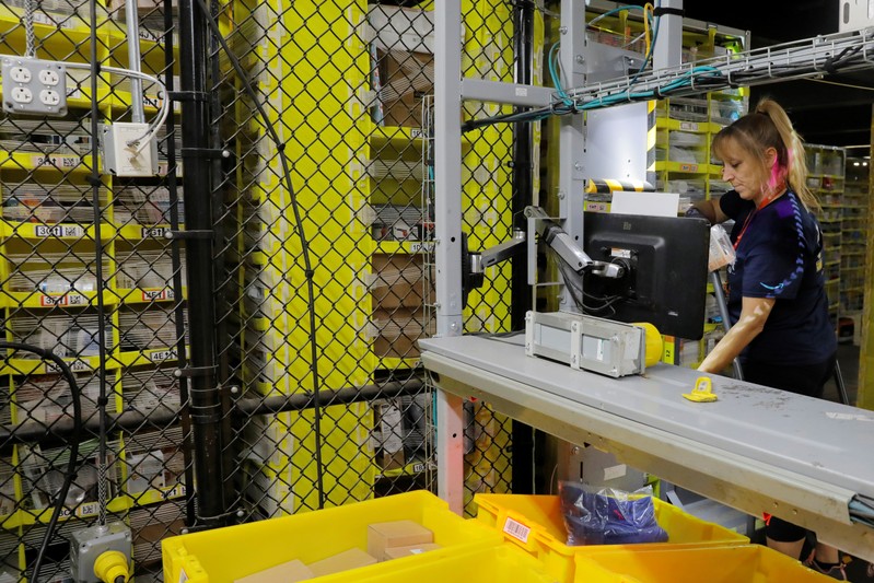 An Amazon employee works to stow items inside of shelves delivered by robots inside of an
