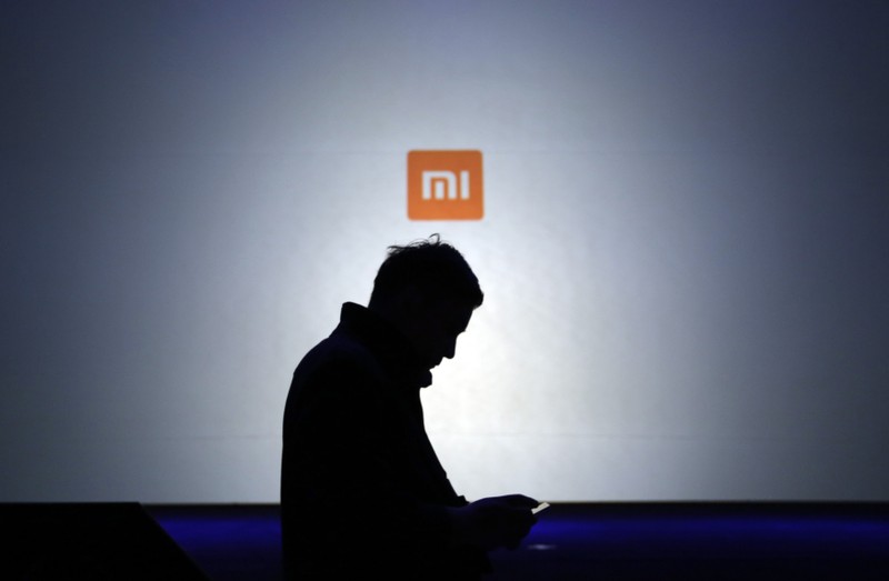 A man uses his mobile phone in front of a screen showing a logo of Xiaomi in Beijing