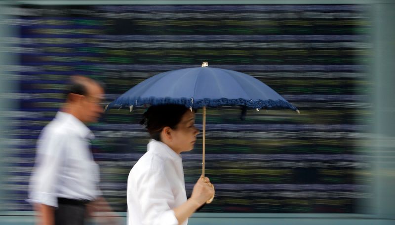 A woman holding a parasol walks past a stock quotation board outside a brokerage in Tokyo