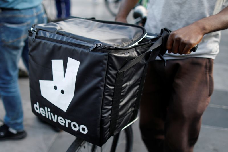 A biker, wearing a Deliveroo food courier backpack, demonstrates during a call on clients to