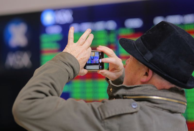 An investor takes a photograph using his phone as he stands in front a board displaying stock