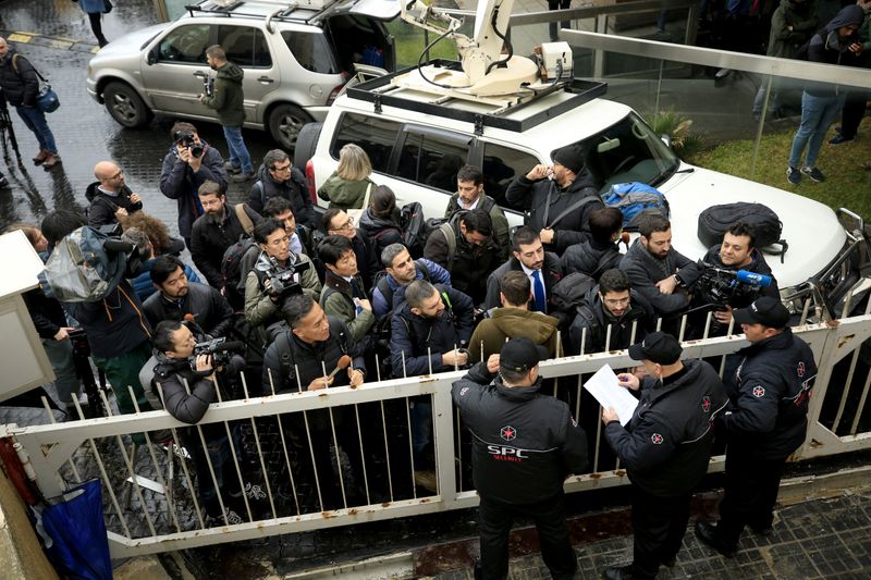 A journalist carries a camera near a car outside the house believed to belong to former Nissan