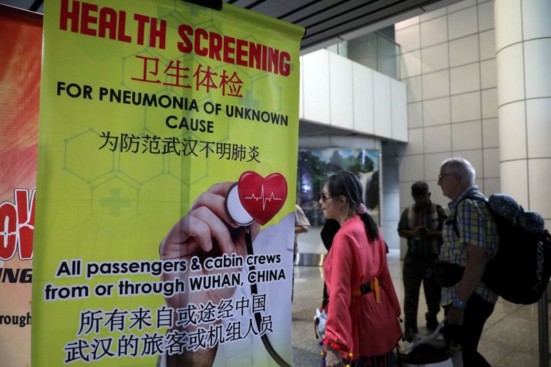 FILE PHOTO: Passengers pass a banner about Wuhan Pneumonia at a thermal screening point in the