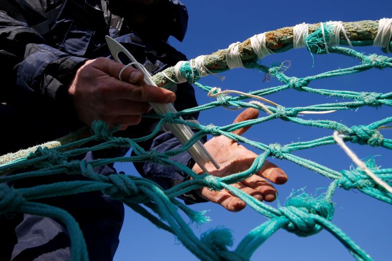 A fisherman repairs a fishing net on the dock of the port in Boulogne-sur-Mer