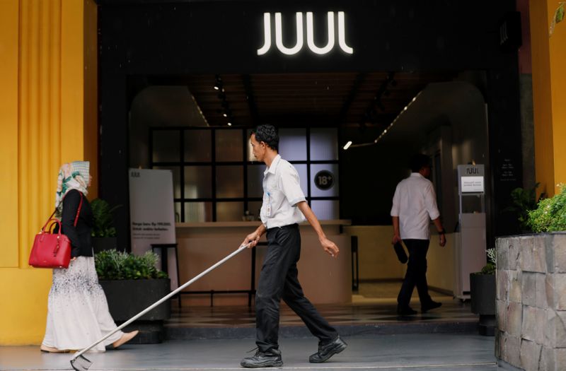 A worker sweeps as people walk pass the Juul shop at a shopping mall in Jakarta