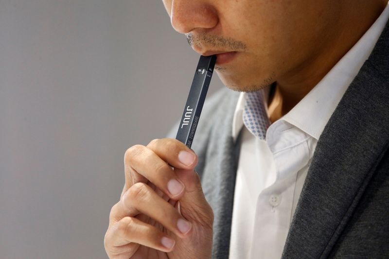 A shopkeeper demonstrates smoking a Juul brand vaping pen to customers at a Juul shop in