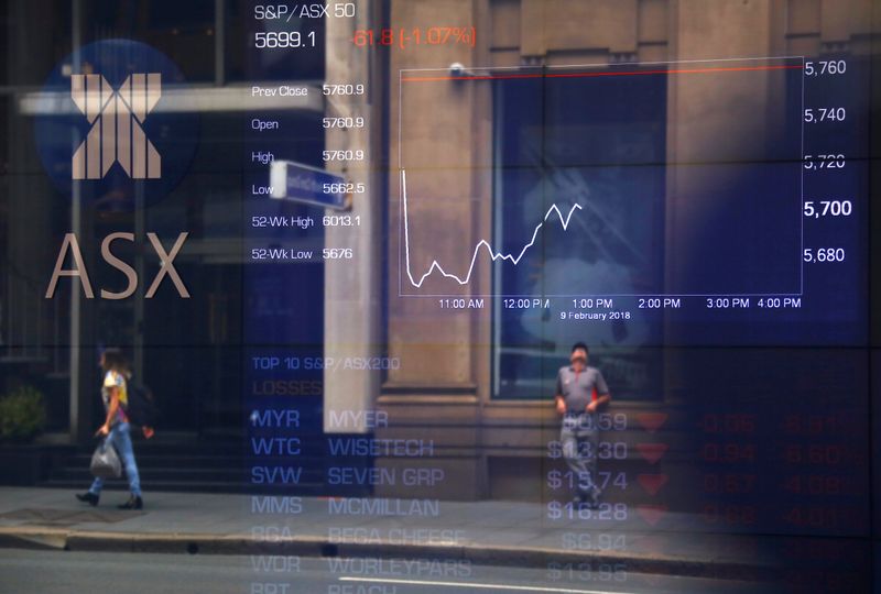 Pedestrians are reflected in a window in front of a board displaying stock prices at the