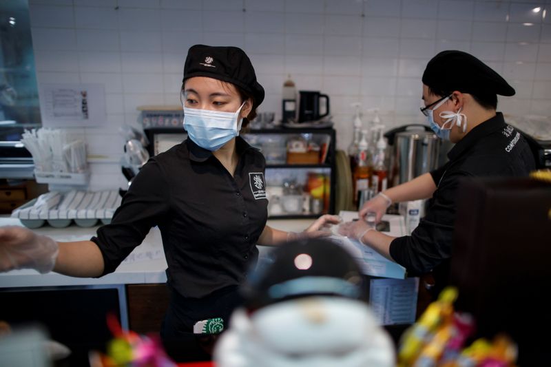 Beautician wearing protective mask and goggles attends to a customer with facial mask during