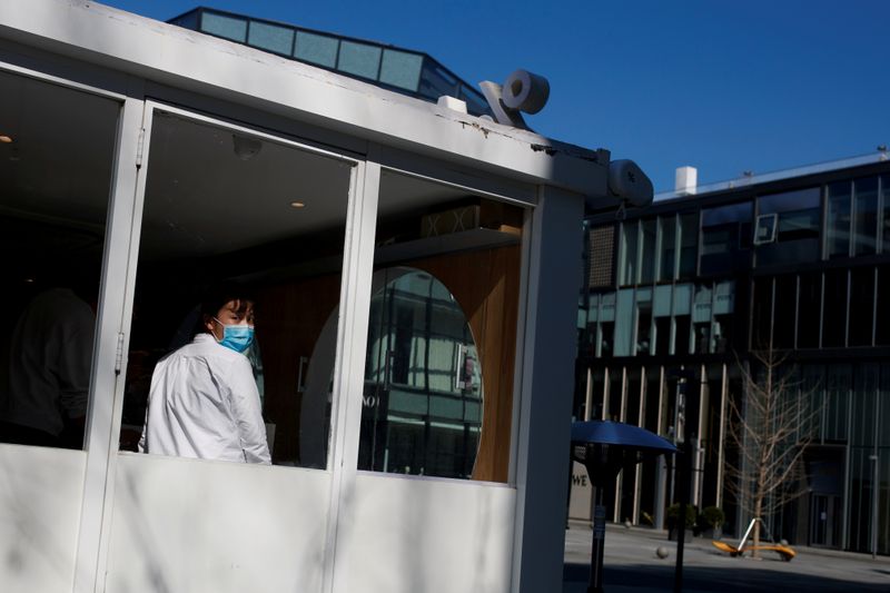 FILE PHOTO: A sales woman wearing a face mask looks out of a coffee shop in an upmarket