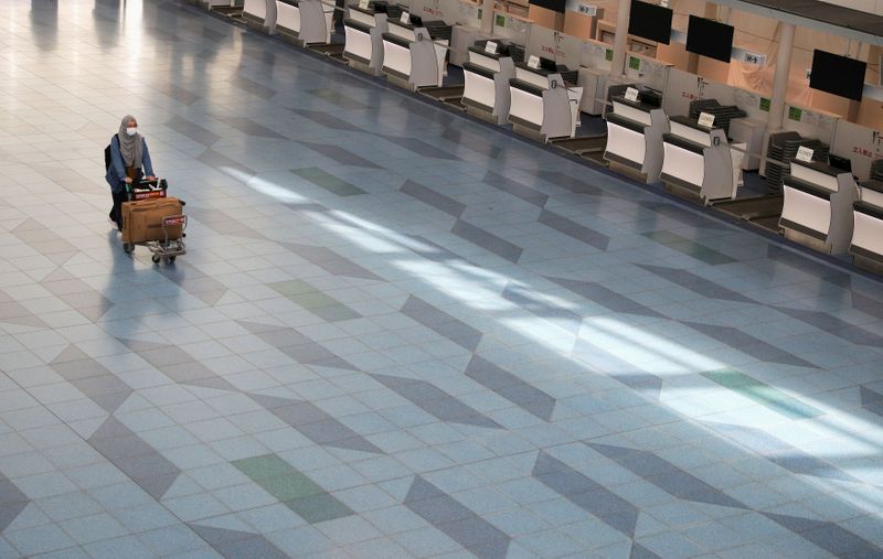 FILE PHOTO: A woman pushes a luggage cart near closed check-in counters at Haneda Airport in