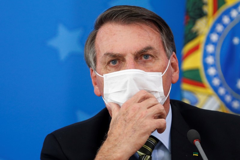 Brazil's President Jair Bolsonaro wearing a protective face masks reacts during a news