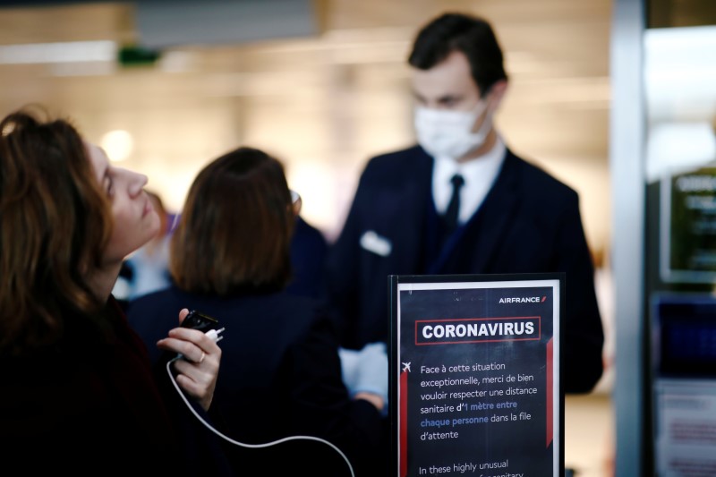 A masked Air France ticket agent helps travellers at Paris Charles de Gaulle airport, following