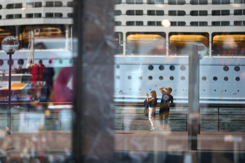Two people, seen in the reflection of a shop window, stand on the mostly deserted waterfront of