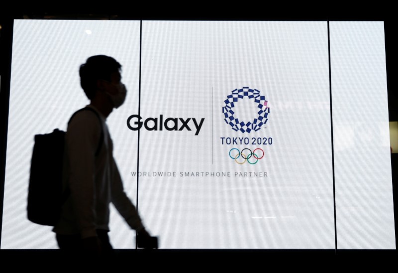 A passerby walks past an electric screen displaying logos of Tokyo 2020 Olympic Games and