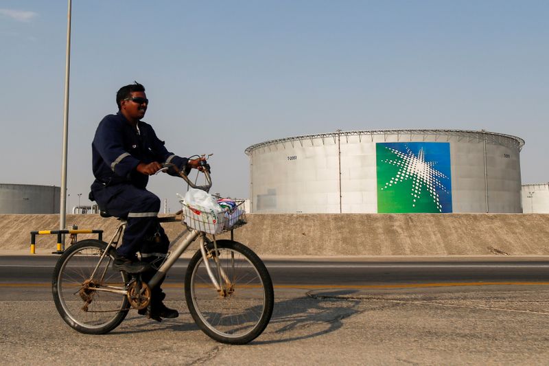 FILE PHOTO: An employee rides a bicycle next to oil tanks at Saudi Aramco oil facility in