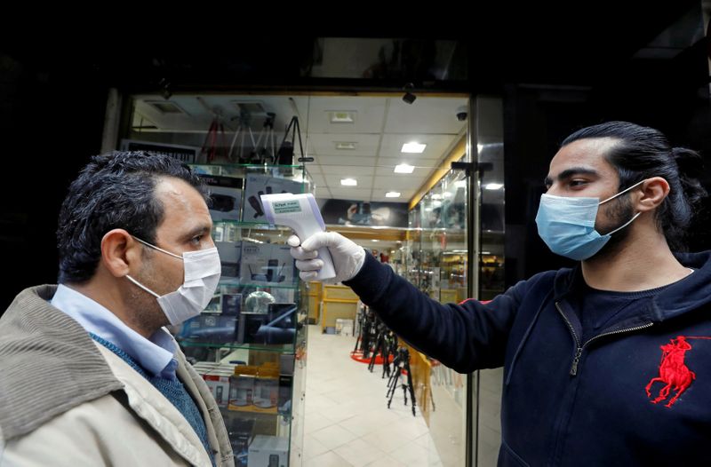 FILE PHOTO: A shop assistant checks customers' temperature before they walk into the store in