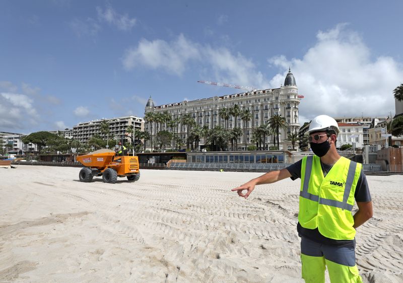 A worker wearing a protective face mask gestures on the beach of the Carlton hotel in Cannes