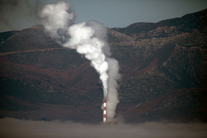 A coal-fired power plant is partially covered by morning fog, next to the town of Megalopoli