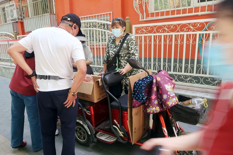 Customers buy fruits from a street vendor at a fruit stall set up outside a residential